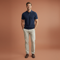 Man wearing a navy polo shirt and beige pants on a brown background